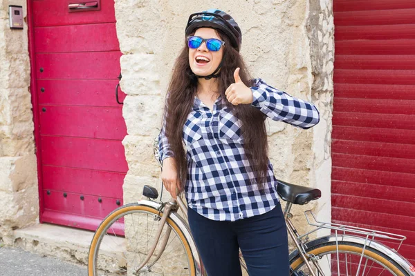 헬멧과 선글라스 빨간 배경 야외에 엄지손가락 보여주는 웃는 여자 — 스톡 사진