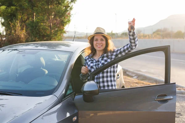 Happy woman driver showing car keys and leaning on car door