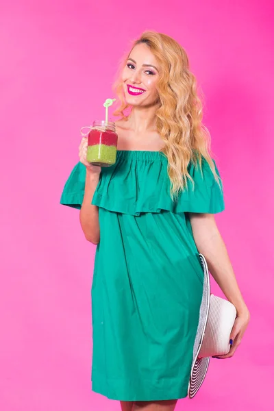 年轻女子在粉红色背景下举行和饮用美味的绿色冰鲜奶昔的画像 — 图库照片