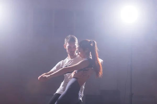 Bailarines hábiles actuando en la sala oscura bajo la luz del concierto y el humo. Pareja sensual realizando una danza contemporánea artística y emocional — Foto de Stock