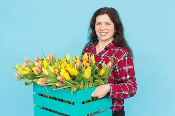 Joyeux jeune femme fleuriste avec boîte de tulipes sur fond bleu — Photo