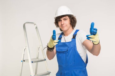 Yakışıklı kamera işaret ve bir merdiven ile infront ayakta beyaz kask Builder'da portresi.