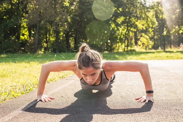 Fitness kobieta robi pompki podczas treningu odkryty przekrojowy. Piękne młode i fit fitness sport szkolenie modelu poza w parku — Zdjęcie stockowe