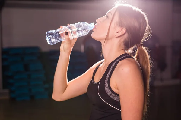 Fitness jeune femme buvant de l'eau de bouteille. Musclé jeune femme à la salle de gym prendre une pause de l'entraînement . — Photo