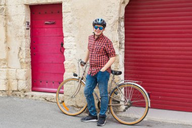 Genç adam, kask, güneş gözlüğü ve kırmızı gömlek tutun Bisiklet artalan kırmızı açık