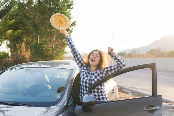 Happy woman driver showing car keys and leaning on car door