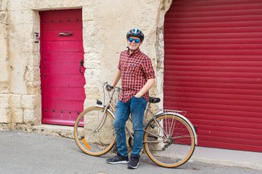 Genç gülümseyen adam, kask, Bisiklet üzerinde açık kırmızı gömlek ve güneş gözlüğü tutun