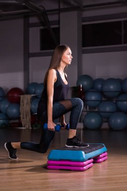 Genç kadın adım kardiyo dumbbells ile bir spor salonunda gerçekleştirir.