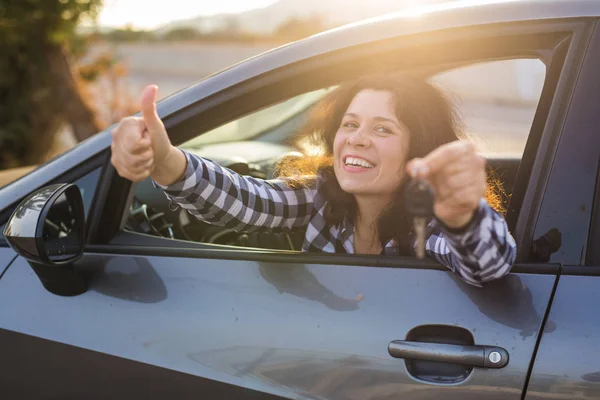 Glückliche junge Frau im Auto mit Schlüssel und Daumen hoch-Geste — Stockfoto