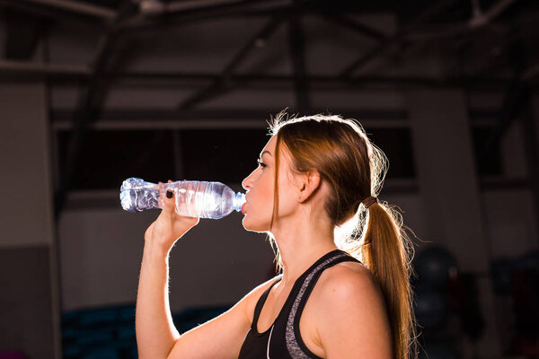 Fitness young woman drinking water in the gym. Muscular woman taking break after exercise