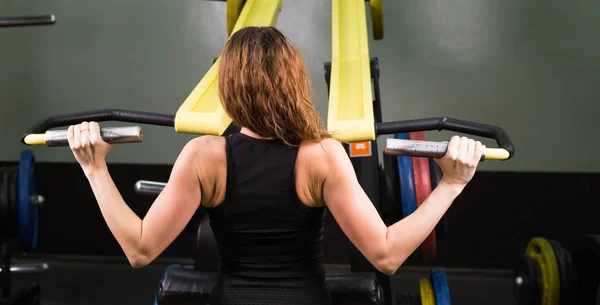 Fitness kvinna köra övningen med träningsmaskin i gym, bakifrån — Stockfoto