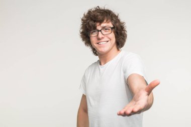 Dostluk, işbirliği ve tebrik kavramı - kıvırcık erkekte gülümseyen bir el için el sıkışma veren beyaz tişört