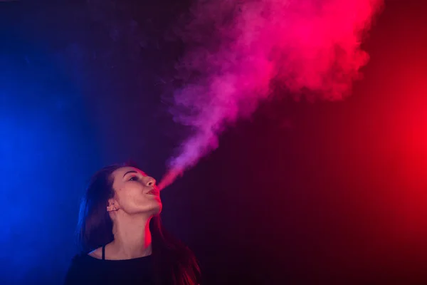 Retrato de mujer joven en humo rojo y azul de neón con vapeo o cigarrillos electrónicos — Foto de Stock