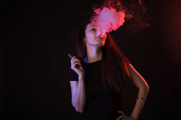 Νεαρή γυναίκα στο φως νέον και τον καπνό του e-τσιγάρα ή vape σε μαύρο φόντο — Φωτογραφία Αρχείου