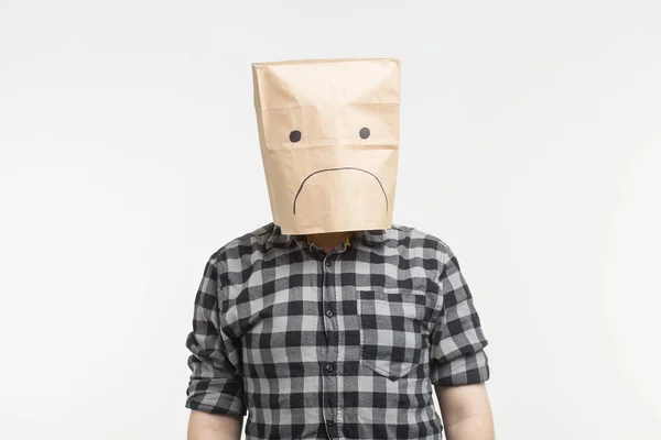 Homem infeliz com emoticon triste na frente de saco de papel em sua cabeça no fundo branco — Fotografia de Stock