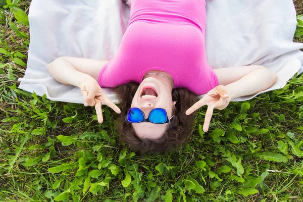 Verano, vacaciones y concepto de diversión - Retrato superior de la joven mujer divertida con gafas de sol tumbado en la hierba en el parque —  Fotos de Stock