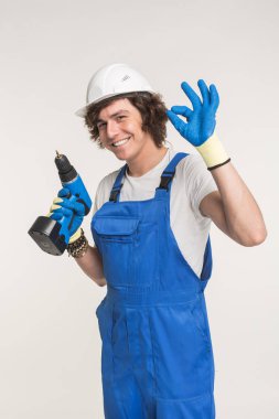 Stüdyo portre mutlu Builder kameraya eldiven ve beyaz kask giyiyor tornavida ile gülüyor.