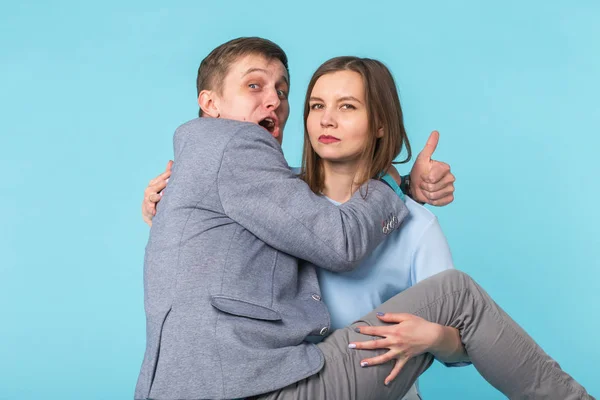 Bromas divertida pareja - chica mantener a su novio en sus manos sobre fondo azul — Foto de Stock