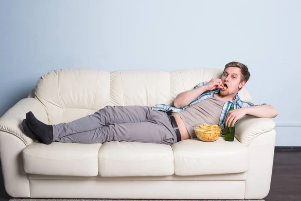 Homem com cerveja e batatas fritas assistindo TV em casa — Fotografia de Stock