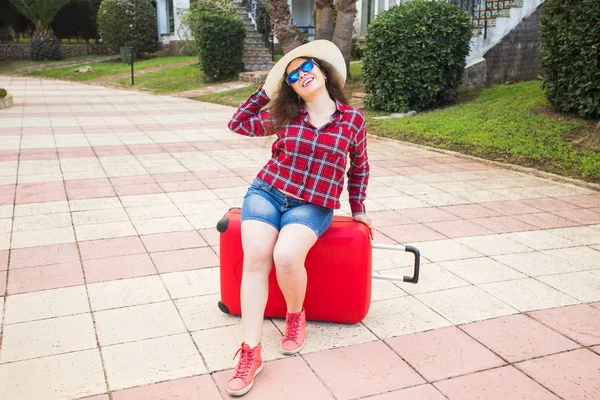 Reise-, Tourismus- und Personenkonzept - glückliches Mädchen auf rotem Koffer mit Brille und Hut auf dem Kopf — Stockfoto