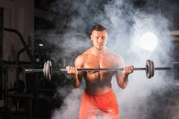 Bodybuilder, der die Übungen mit der Langhantel macht. kräftiges Männchen mit nacktem Oberkörper auf dunklem Hintergrund. Stärke und Motivation. — Stockfoto
