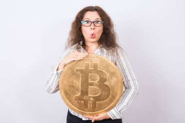 Kamera seyir ve büyük altın bitcoin beyaz arka plan üzerinde tutarak açık ağızlı sürpriz iş kadını