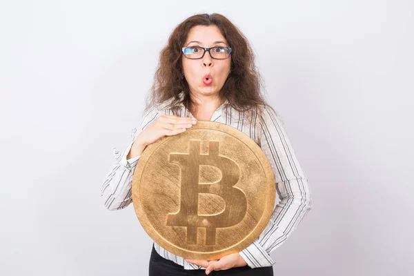 Mujer de negocios sorprendida con la boca abierta mirando cámara y sosteniendo gran bitcoin de oro sobre fondo blanco — Foto de Stock