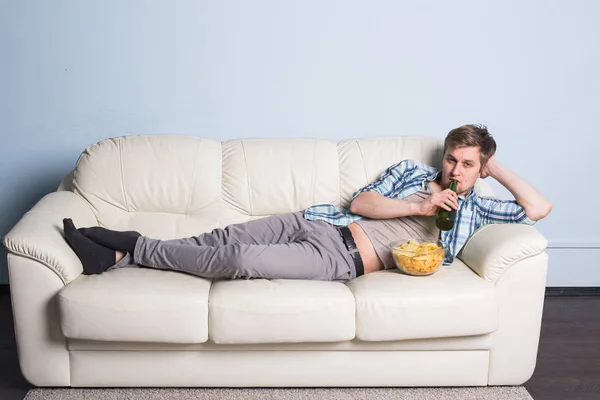 Homem com cerveja e batatas fritas assistindo TV em casa — Fotografia de Stock