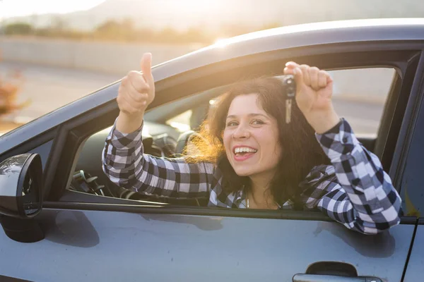 Menina feliz em um carro mostrando uma chave e polegar acima gesto — Fotografia de Stock