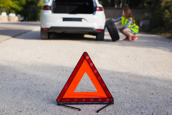 Sinal triangular do acidente no fundo de uma menina prestes a mudar a roda — Fotografia de Stock