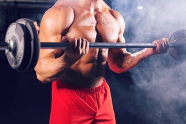 Barbell ile egzersizleri yapıyor vücut geliştirmeci, yakın çekim. Koyu arka plan üzerinde çıplak gövde ile güçlü erkek. Güç ve motivasyon.