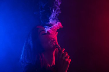 Neon ışık ve duman e-sigara veya vape koyu arka plan üzerinde genç kadın