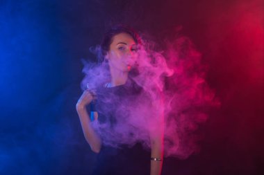 Neon ışık ve duman e-sigara veya vape koyu arka plan üzerinde genç kadın
