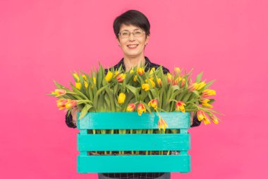 Mutlu güzel esmer beyaz orta yaşlı bir kadın ile lale pembe bir arka plan üzerinde büyük kutu.