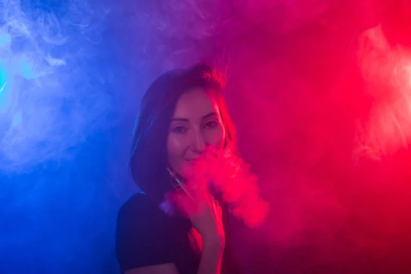 穿黑色 t恤衫的年轻女子 vaping 红蓝霓虹灯 — 图库照片