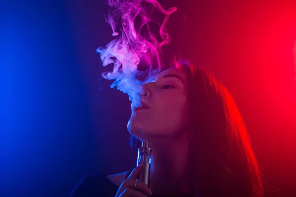 Jovem mulher em t-shirt preta vaping em luz de néon vermelho e azul — Fotografia de Stock