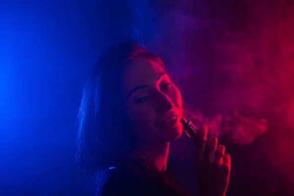 Mujer joven que fuma vapor o cigarrillo electrónico en luz de neón —  Fotos de Stock