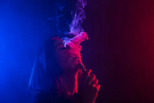 Mladá žena v neonové světlo a kouření e cigaret nebo vape na tmavém pozadí — Stock fotografie