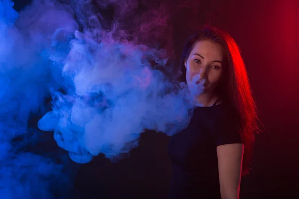 Giovane donna in t-shirt nera vaping in luce al neon rossa e blu — Foto Stock