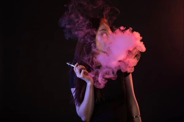 Молодая женщина в неоновом свете и дыма электронных сигарет или vape на черном фоне — стоковое фото