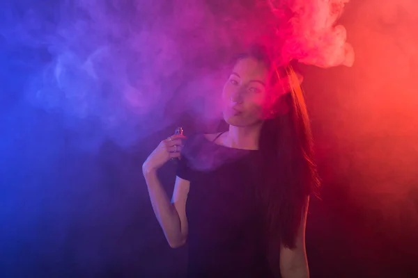 Retrato de mulher asiática fumando vape ou e-cigarro em luz de néon em fundo preto . — Fotografia de Stock