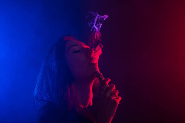 Young woman in black t-shirt vaping in red and blue neon light
