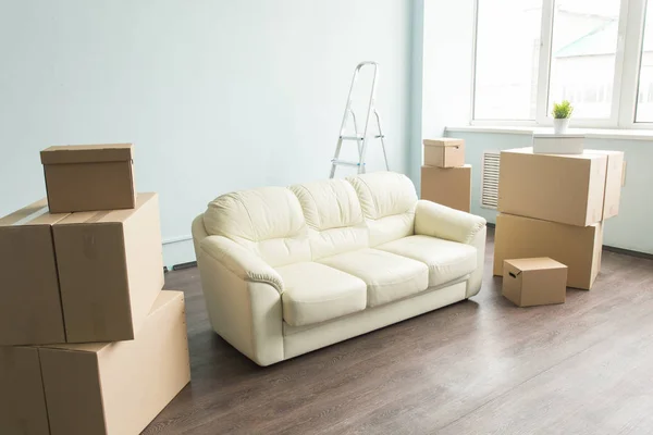 Новый дом, отдых, переезд, концепция мебели - новый белый диван в пустой комнате между множеством коробок — стоковое фото