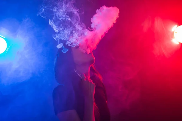 Young woman in black t-shirt vaping in red and blue neon light