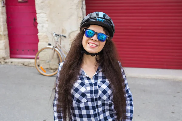 Весела жінка з сонцезахисними окулярами та шоломом на фоні червоних дверей та велосипеда — стокове фото