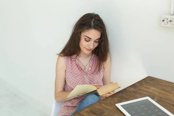 Lettura, educazione, cultura, concetto di persone: una giovane studentessa legge un libro, mentre è seduta su una sedia bianca in una stanza bianca — Foto Stock