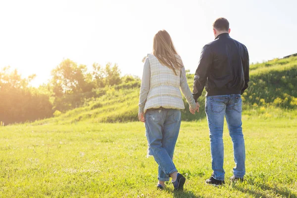 Вид сзади на пару, держащуюся за руки и гуляющую по осенней сельской местности — стоковое фото