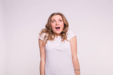 Kıvırcık sarı saçlı beyaz arka plan üzerinde merak ve beyaz t-shirt giyen mutlu beyaz genç kadın portresi