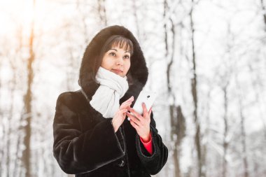 Teknoloji, insan ve kış konsepti - smartphone ve kış manzara kar taneleri arka planda olan kadın