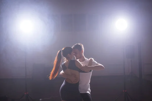 Bailarines hábiles actuando en la sala oscura bajo la luz del concierto y el humo. Pareja sensual realizando una danza contemporánea artística y emocional — Foto de Stock